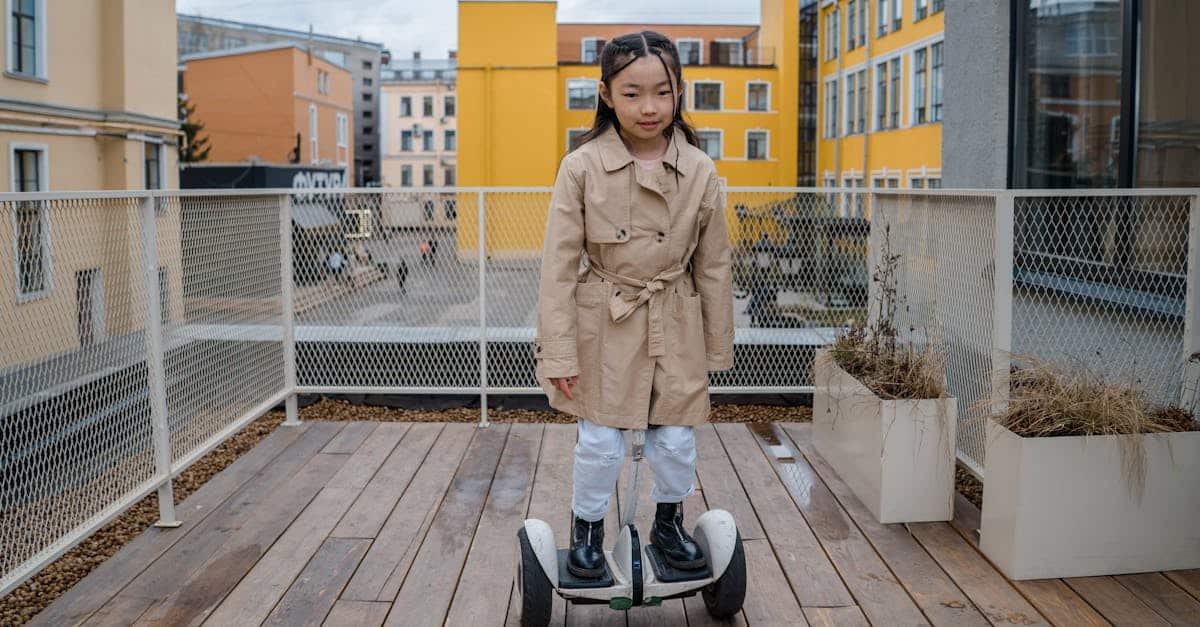 Ein junges Mädchen in einem beigen Trenchcoat und weißen Hosen fährt auf einem weißen Hoverboard auf einem Holzdeck mit Gebäuden im Hintergrund.